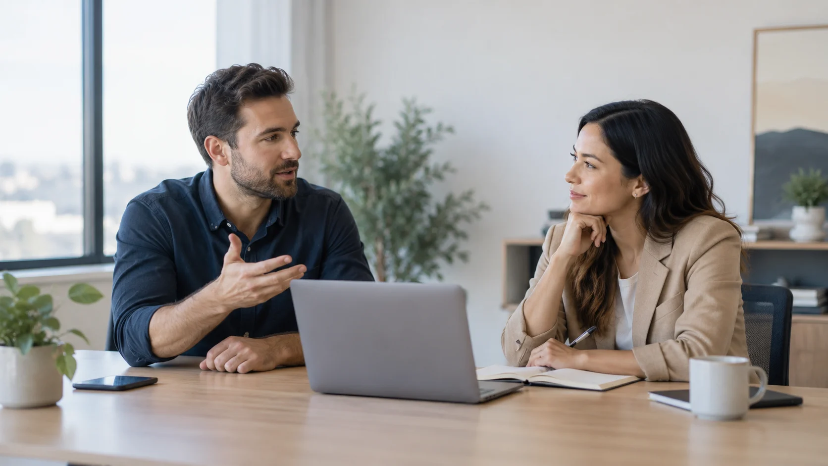 Two professionals discussing an idea beside a laptop and notebook in a modern office.