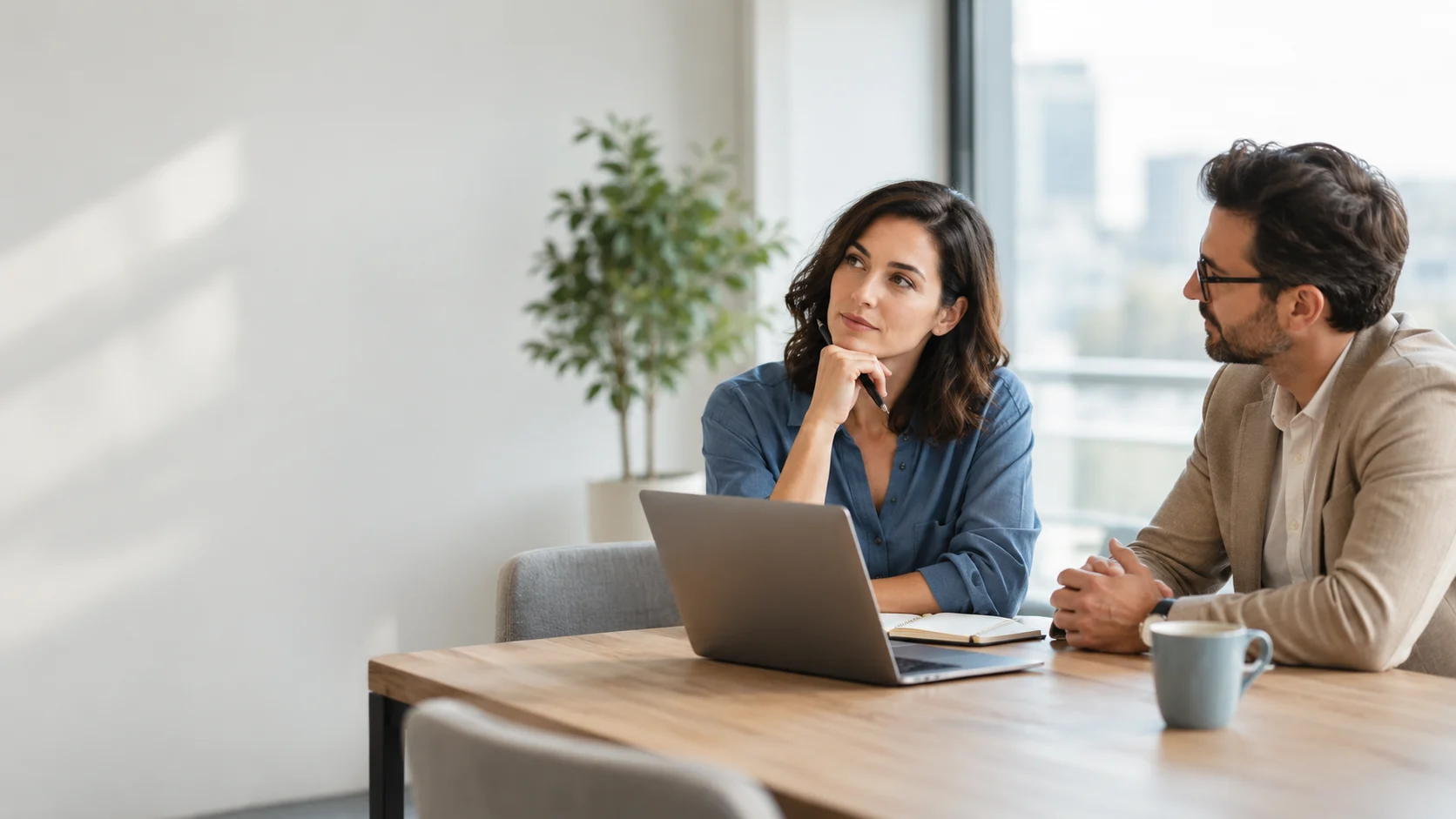 Two colleagues discussing an idea beside a laptop and notebook in a modern office